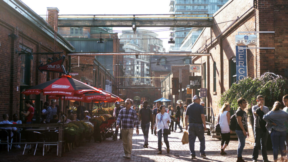 Daytime view of street lined with shops and people eating on patios The Distillery District