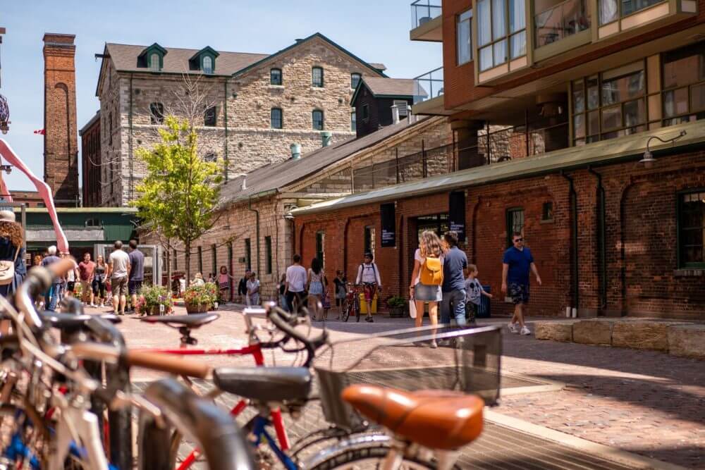 Street level view of west entrance to Distillery District showing brick buildings, people walking and a row of bikes.