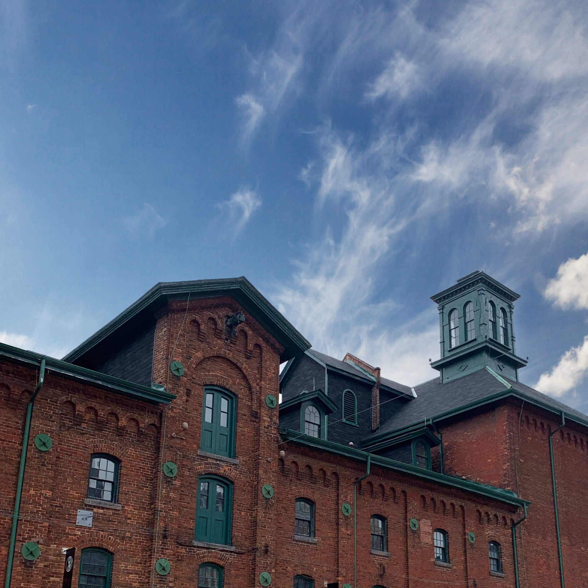 Blue Sky image with the top of Distillery District red brick building with green toned roofing.