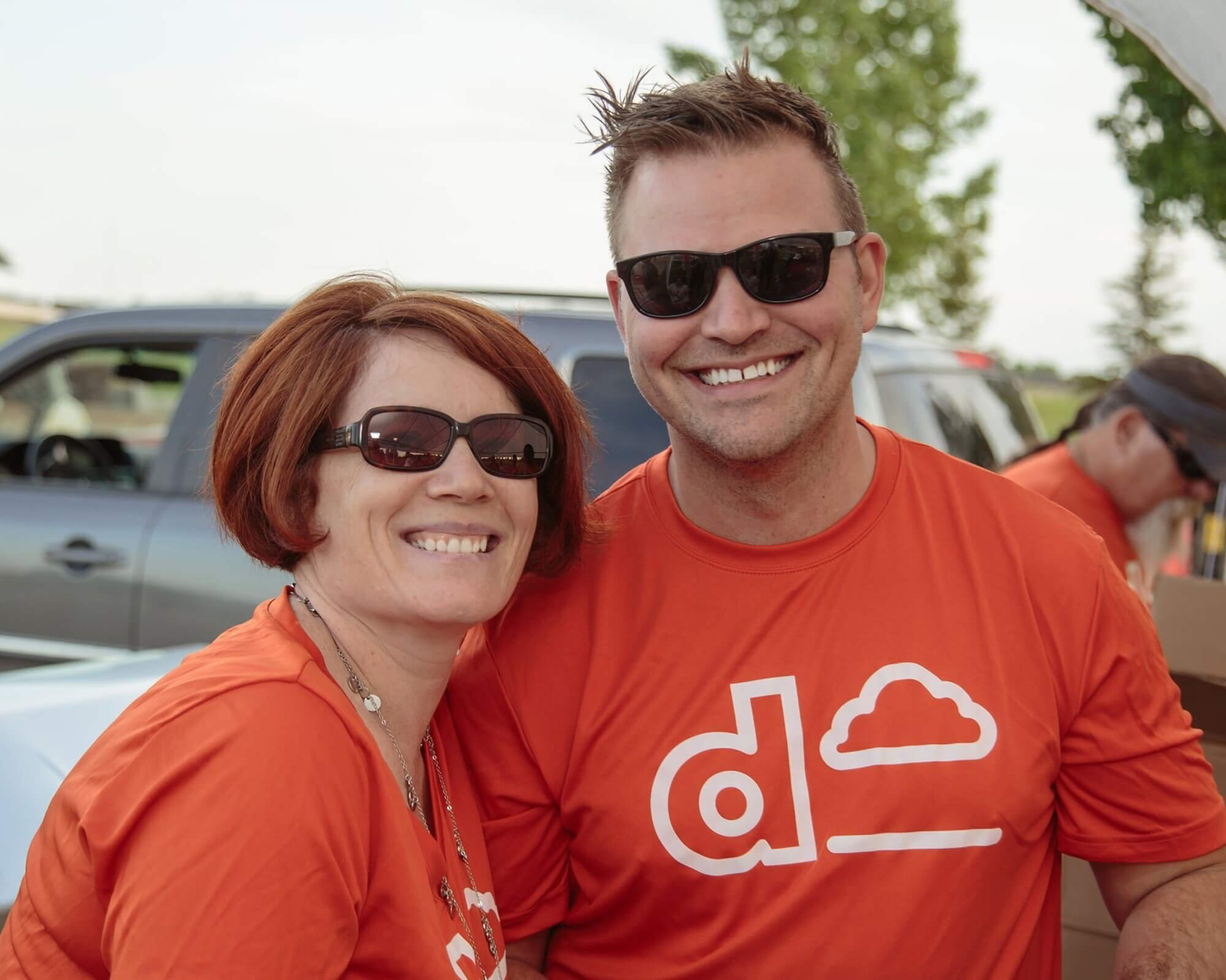Two Dream Employees wearing orange shirts with the Dream logo smiling while volunteering at a charity organization.