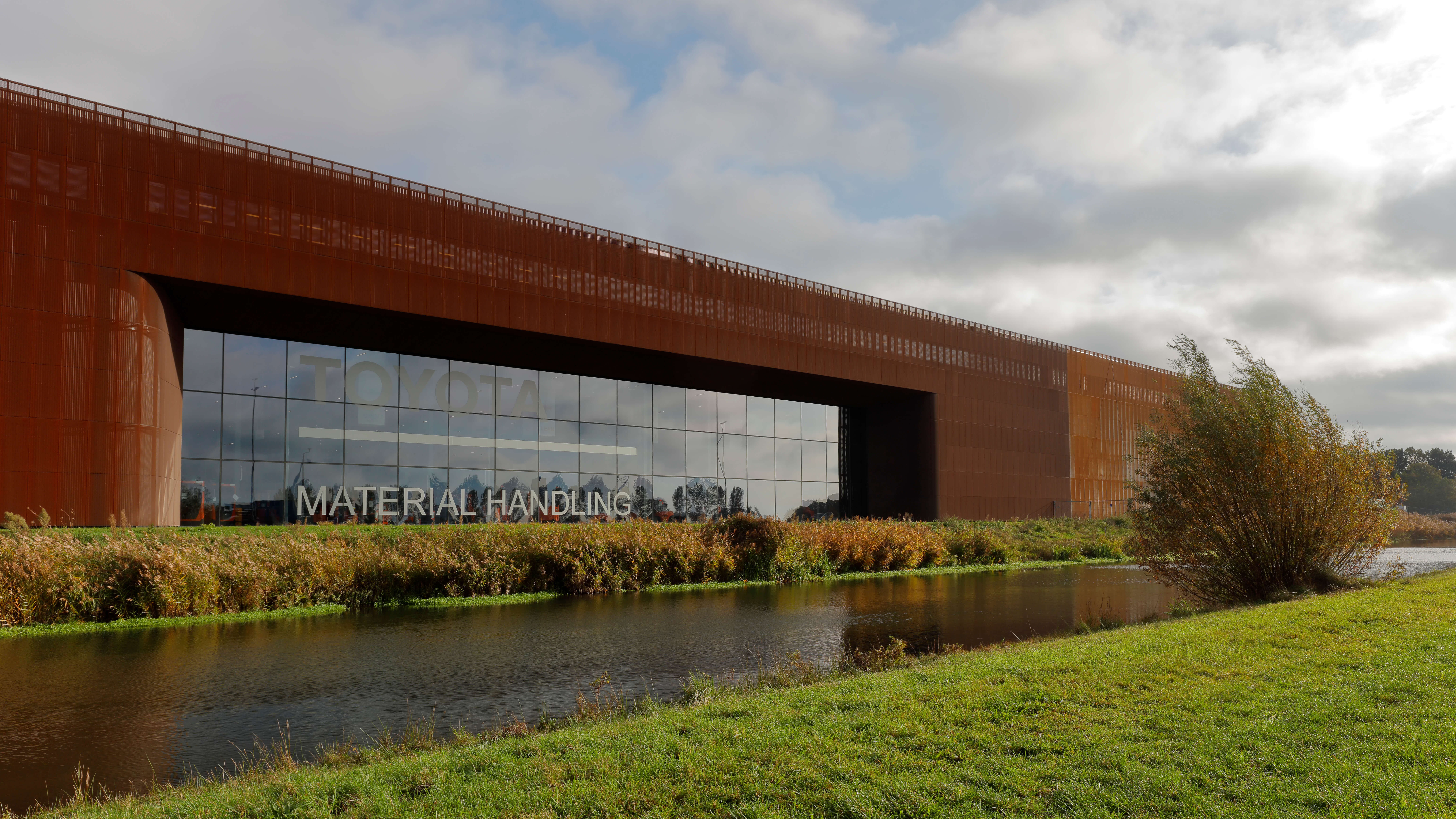 Dream Industrial Building in Ede, Netherlands on a cloudy day beside the river with green grass.