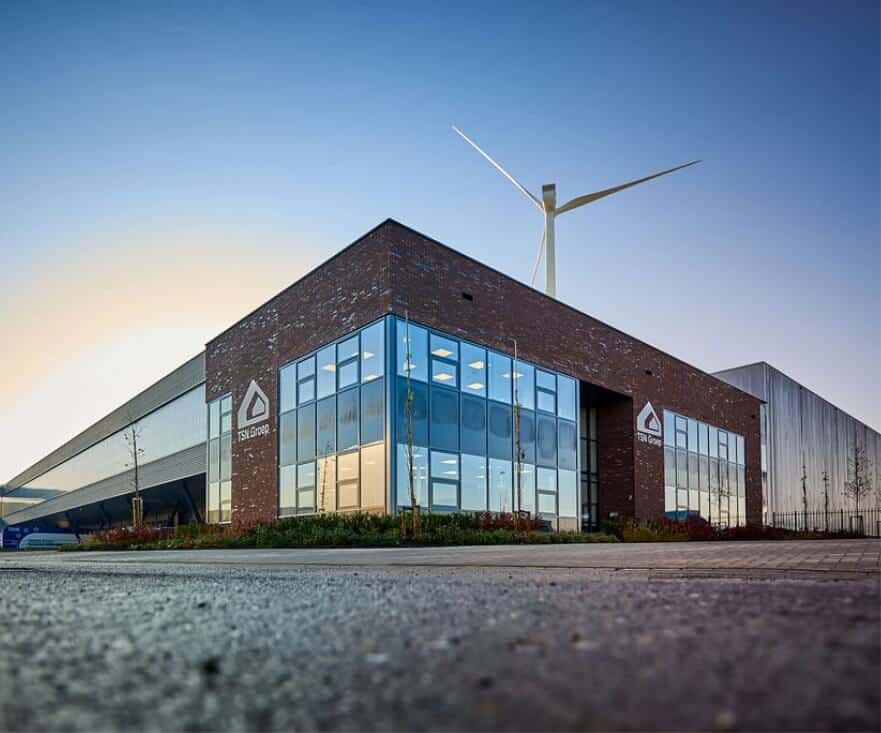 a Dream Development, an industrial brick building with tall glass windows under a bright blue sky as the wind-turbine pokes through the center of the image