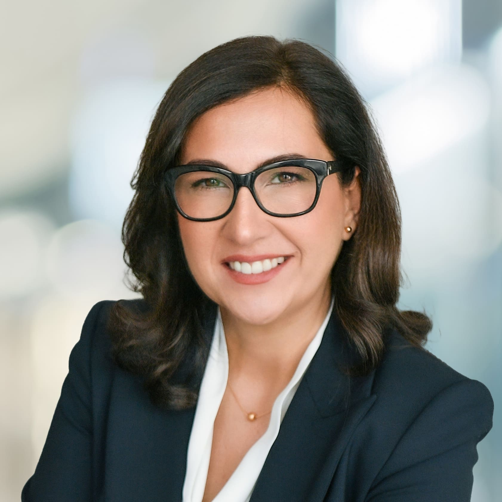 Smiling headshot of Ana Bailao, wearing glasses and a blazer, Head of Affordable Housing and Public Affairs, she is wearing glasses and a blazer.