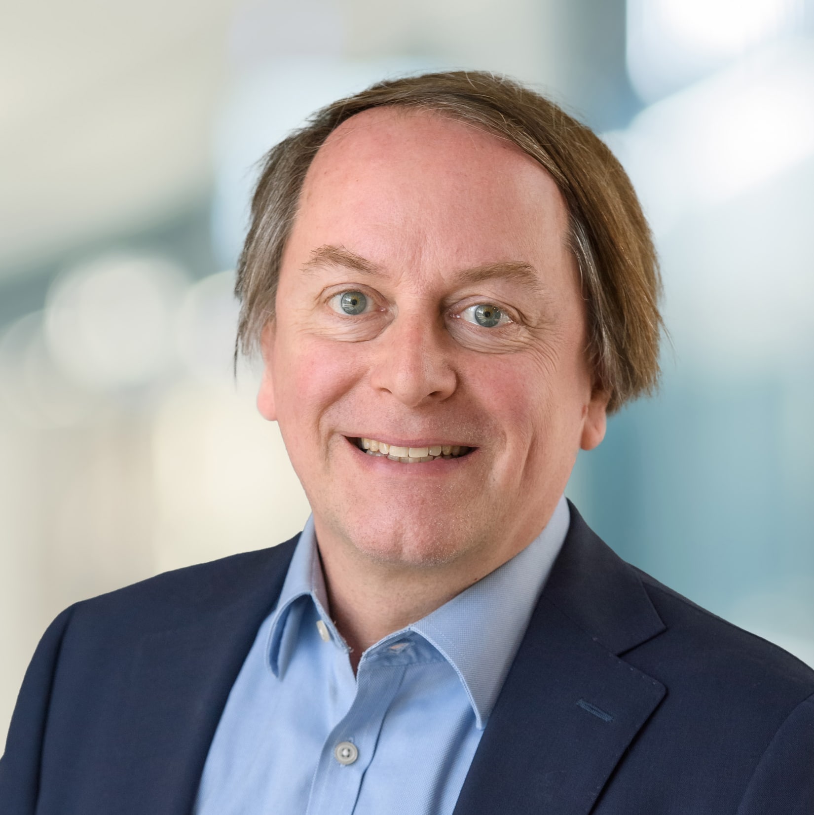 Smiling Headshot of Bruce Investments, Dream Industrial, he wears a blue shirt with an open collar and deep blue jacket.