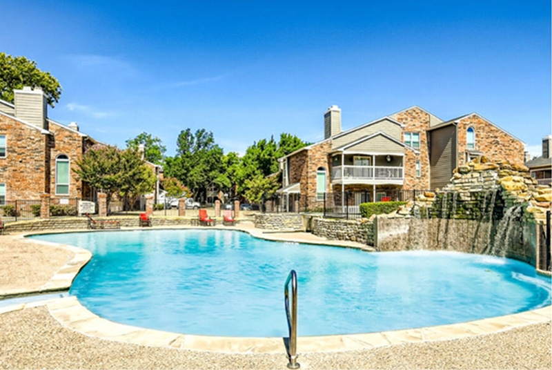 Tall brick houses over look a scenic pool surrounded by lush greenery