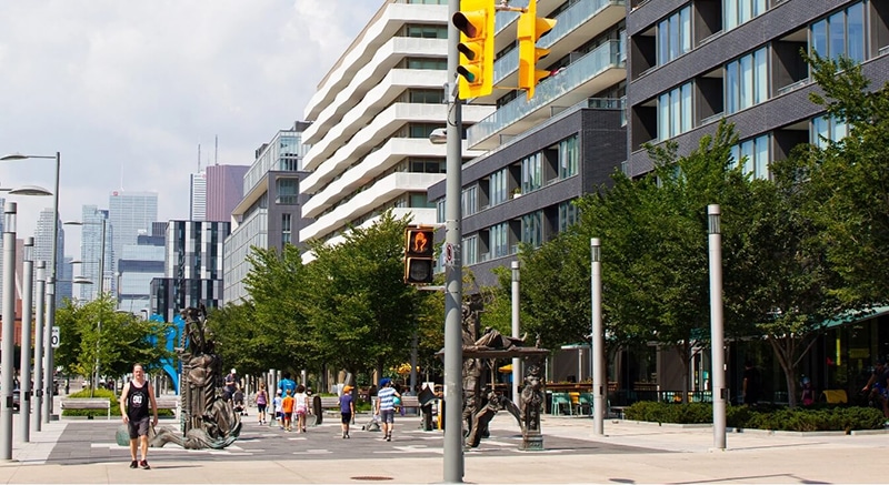 a group families and indivuals dressed in summer apparel, strolling down a bustling street, enjoying each other's company and the vibrant summer city atmosphere, in the Canary district.