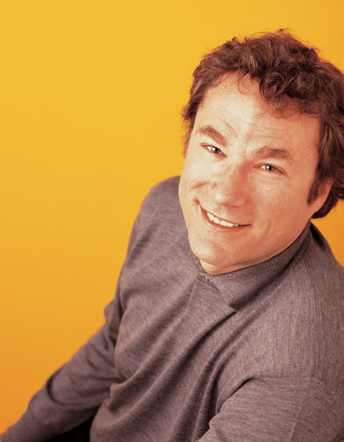 Photo of Michael Cooper, CRO and President of Dream, looking up and smiling wearing a grey button up against a yellow backdrop